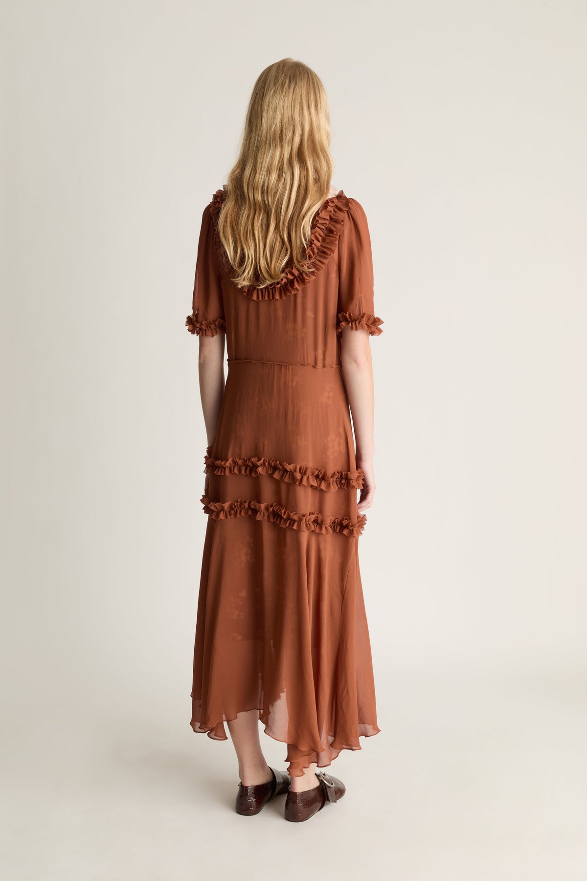 Woman wearing a brown dress with ruffled details on a white background