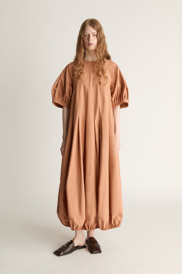 Front view of a woman wearing a long orange dress with puff sleeves  on a white background