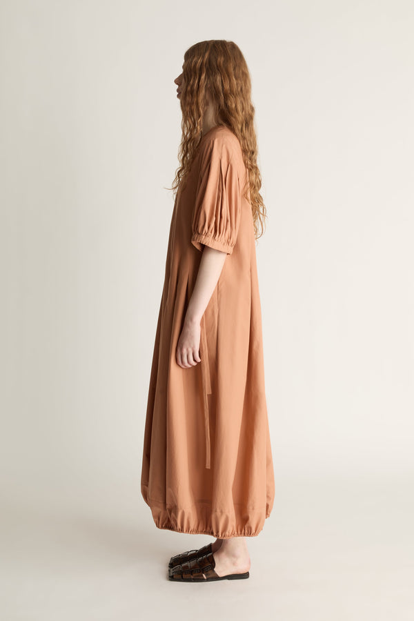 Side view of a woman wearing a long orange dress against a plain background
