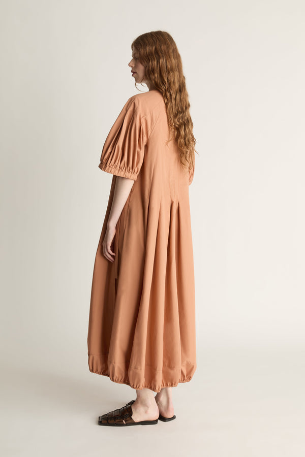 Back view of a woman wearing a long, light brown dress with puff sleeves on a plain background