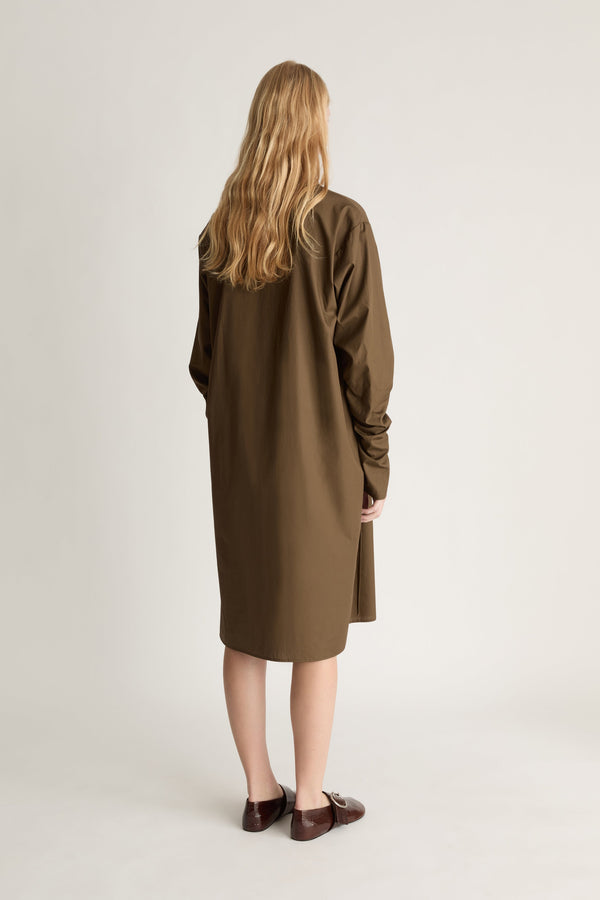 Back view of a person wearing a long brown coat standing against a plain background