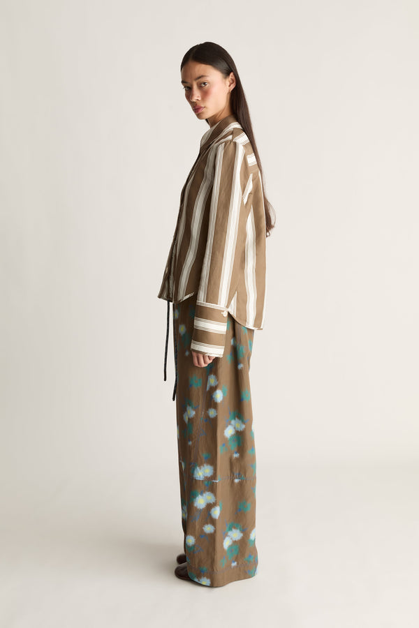 Model wearing Tennant LS shirt— brown vertical-stripe shirt paired with brown floral-print wide-leg trousers, side profile