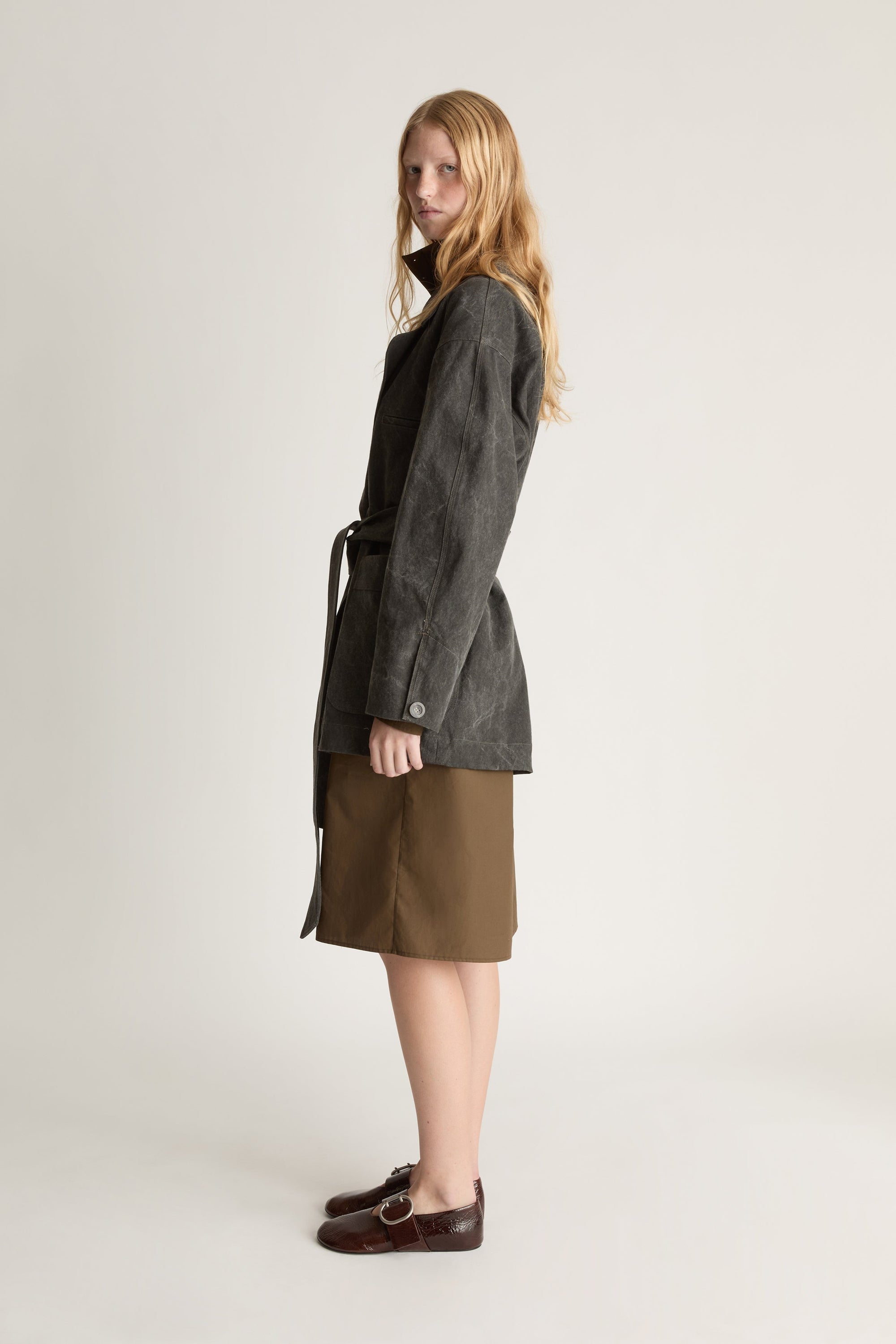 Side view of a woman wearing a gray coat over a green skirt on a white background