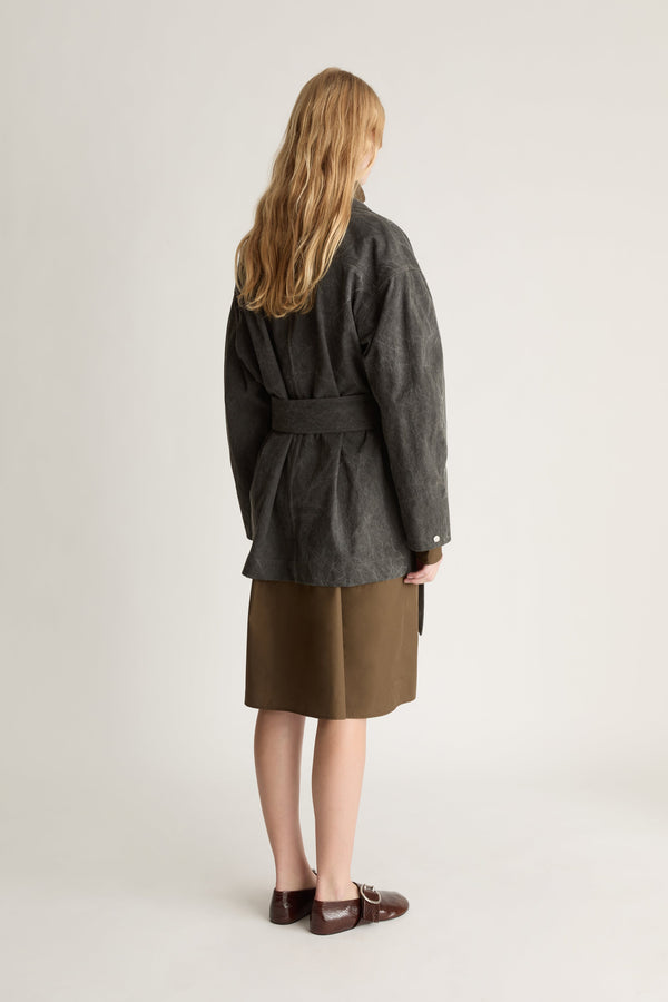 Back view of a woman wearing a grey coat over a khaki skirt against a white studio background.
