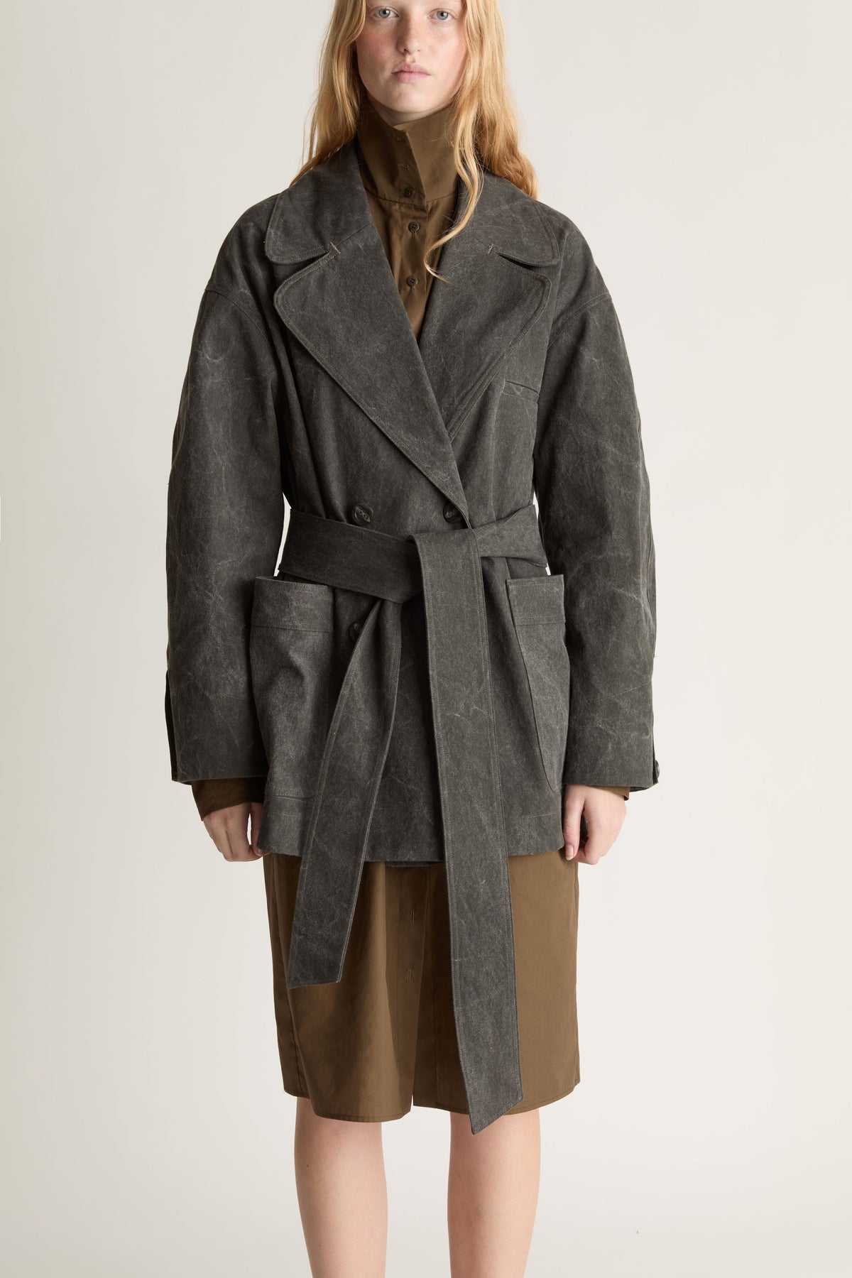 Close up of a woman wearing a grey pea coat over a khaki skirt against a white studio background