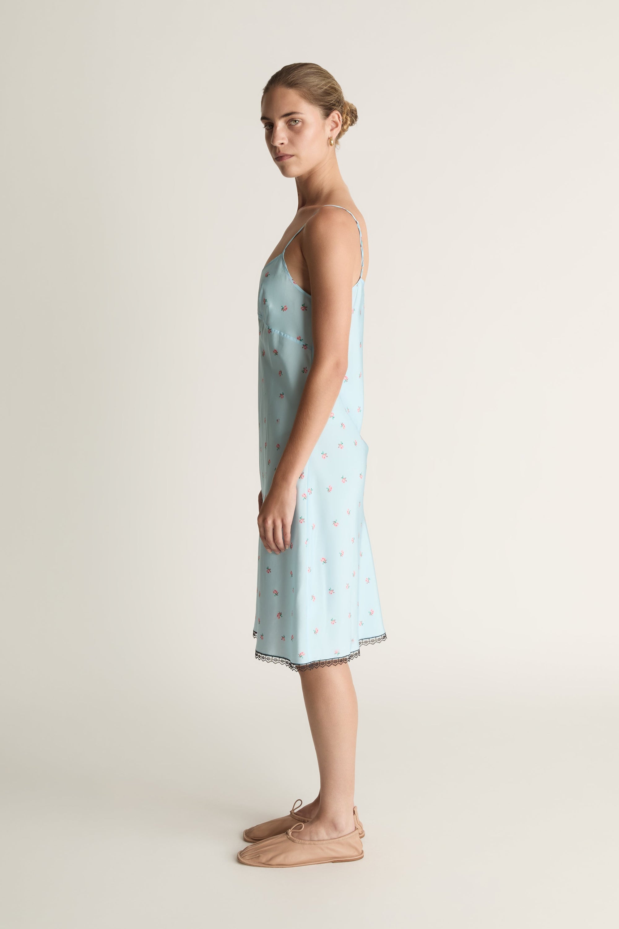 Woman wearing a light blue slip dress with a subtle pattern on a plain background