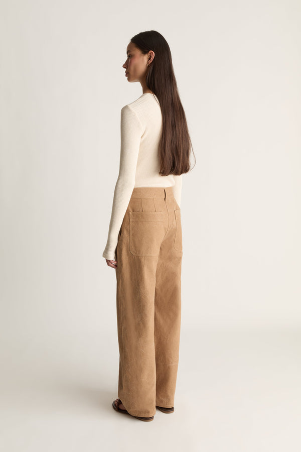 A woman shown from the back wearing a cream long-sleeve top and tan wide-leg canvas trousers against a plain light gray studio background.