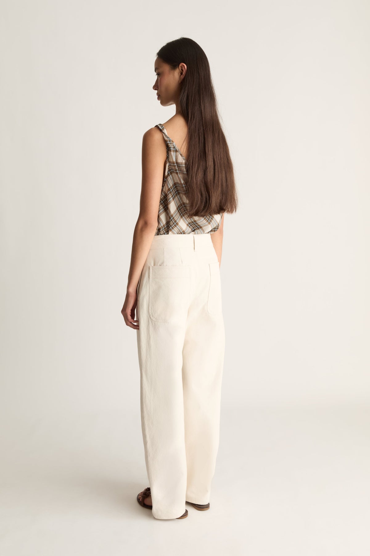 A woman shown from the back wearing a sleeveless plaid top and wide-leg cream canvas trousers against a plain light background.