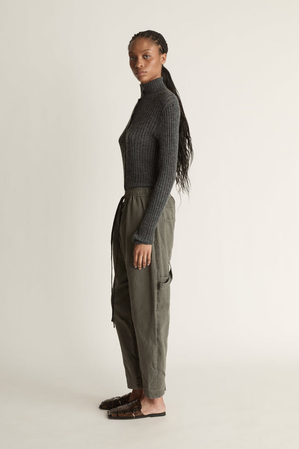 Person wearing a dark gray ribbed long-sleeve top and light gray pants on a white background