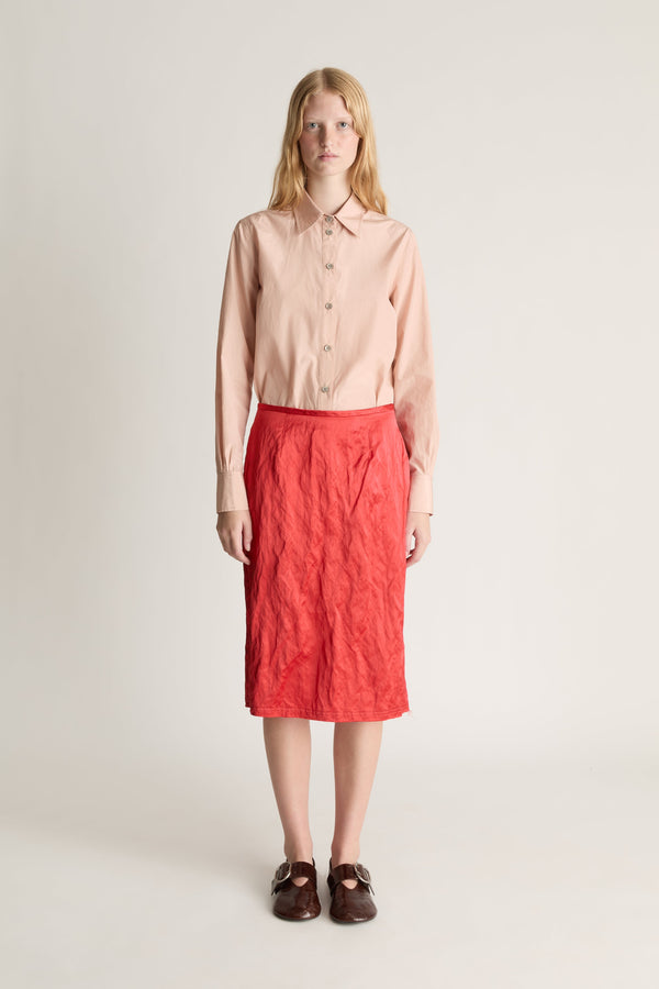 Front view of a woman wearing a pale pink button up shirt and a red silk midi skirt against a white studio background
