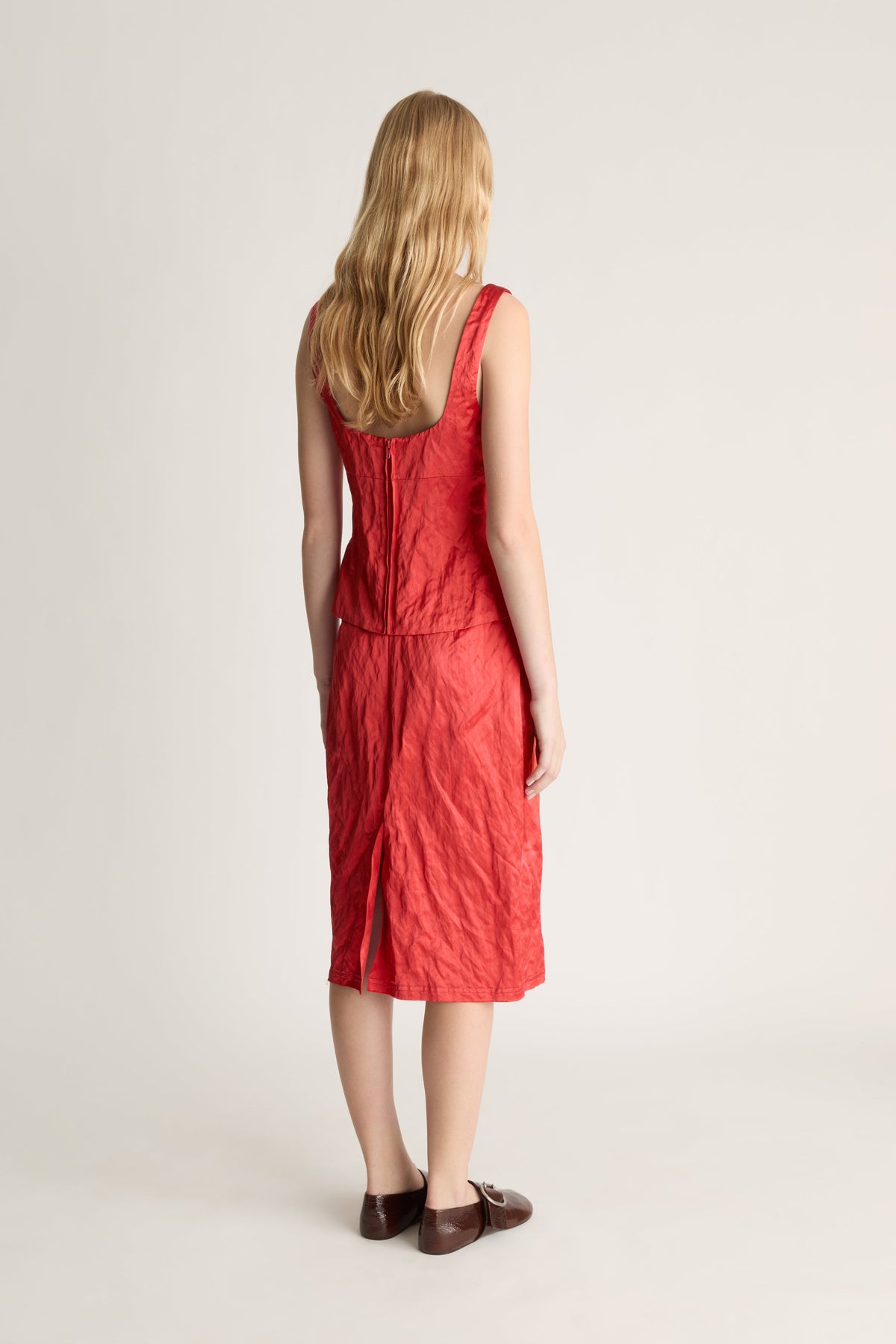 Woman shot from the back wearing a red silk midi skirt and tank top against a white studio background. 