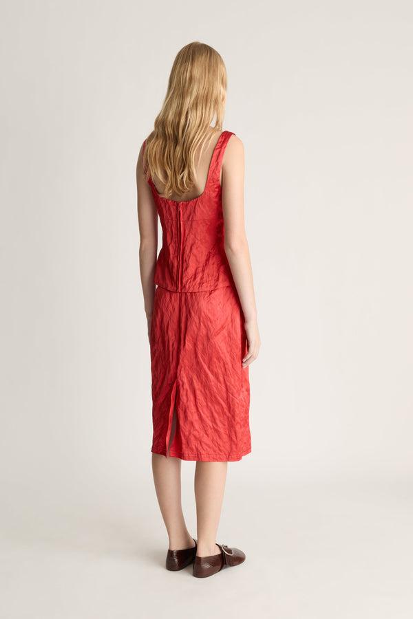 Woman shot from the back wearing a red silk midi skirt and tank top against a white studio background. 