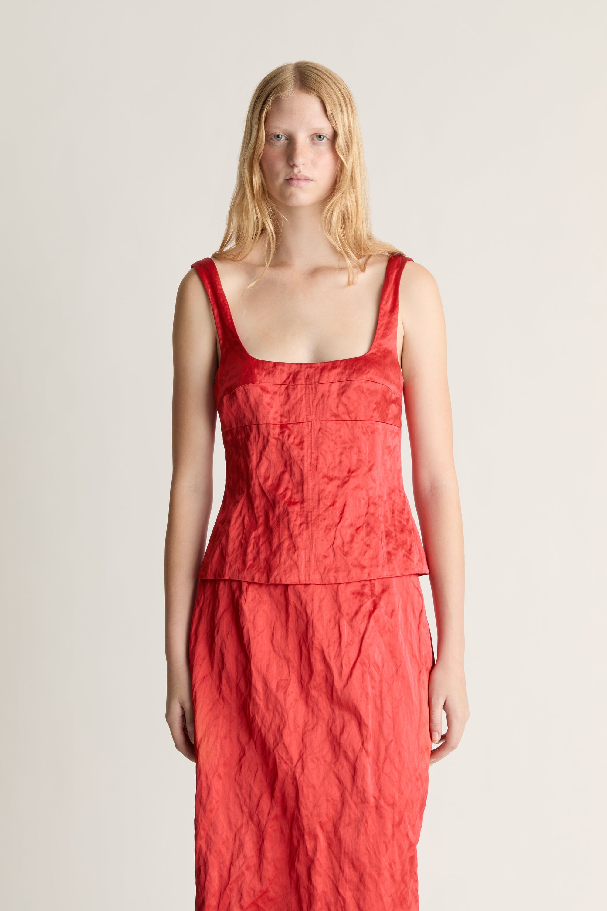 Woman wearing a red silk tank top and midi skirt against a white studio background. 