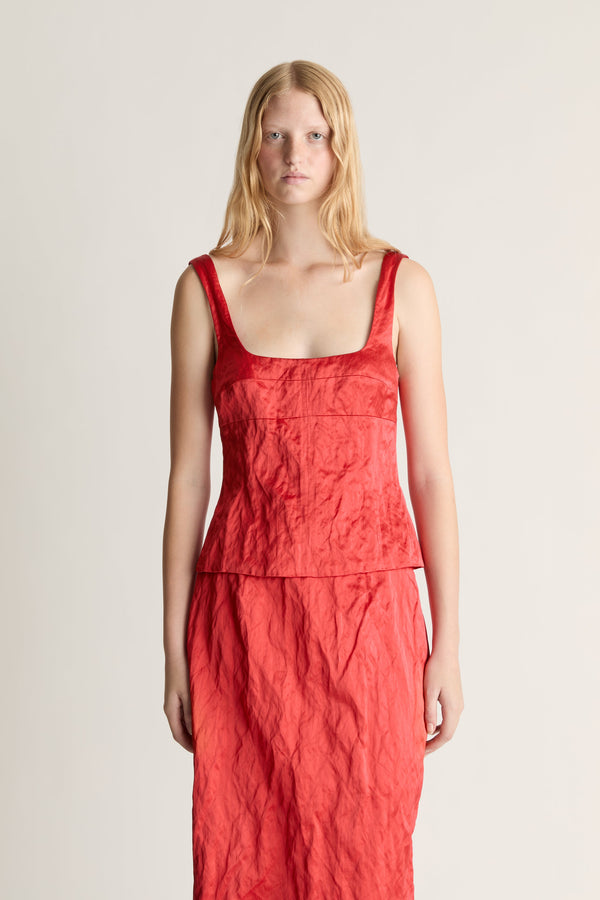 Woman wearing a red silk tank top and midi skirt against a white studio background. 