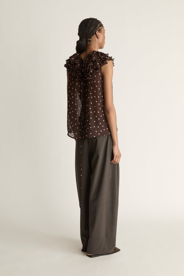 Woman wearing a brown polka dot top and dark pants on a white background