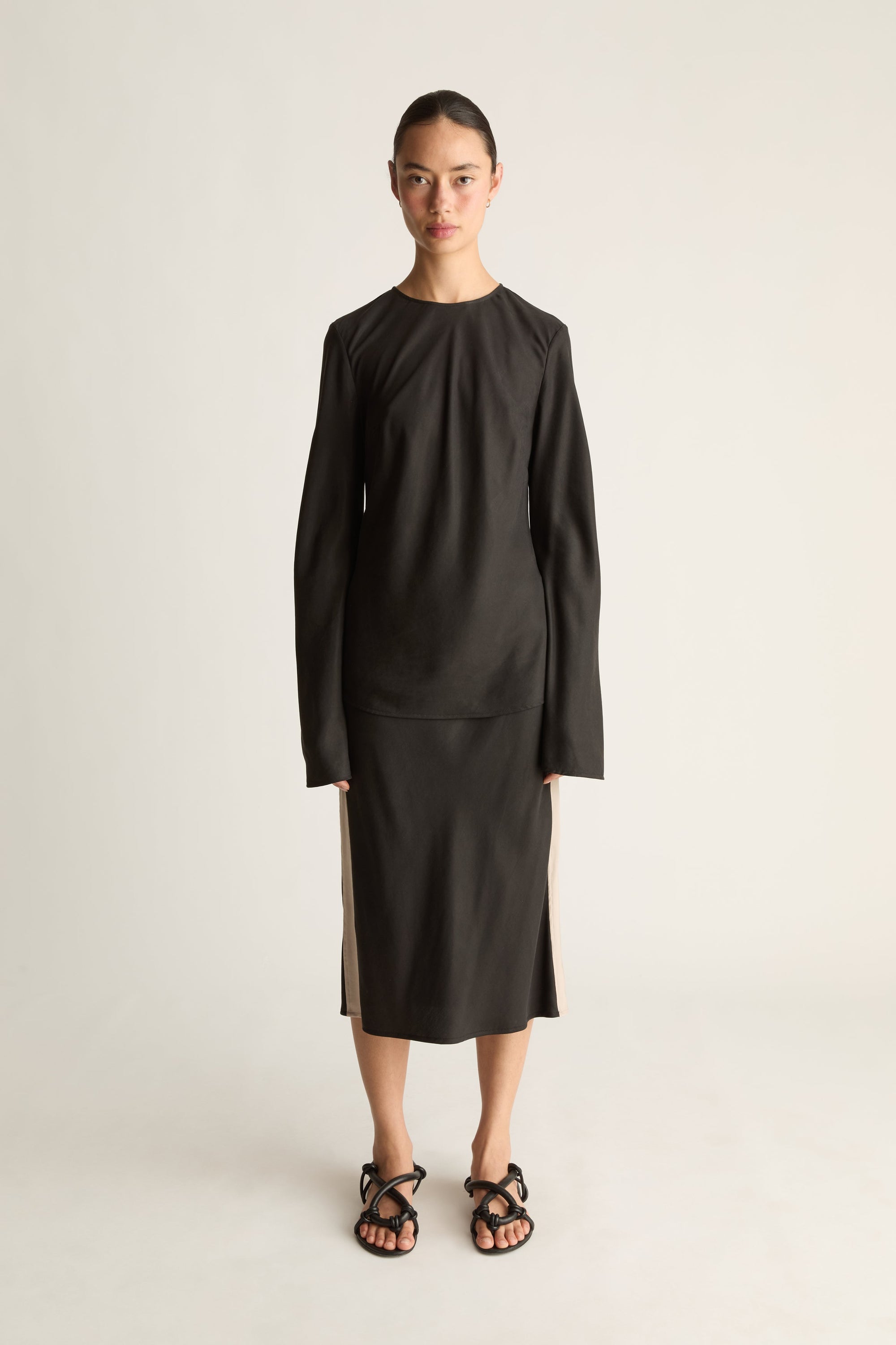 Front view of a woman wearing a black long sleeve shirt with a black skirt against a white studio background.