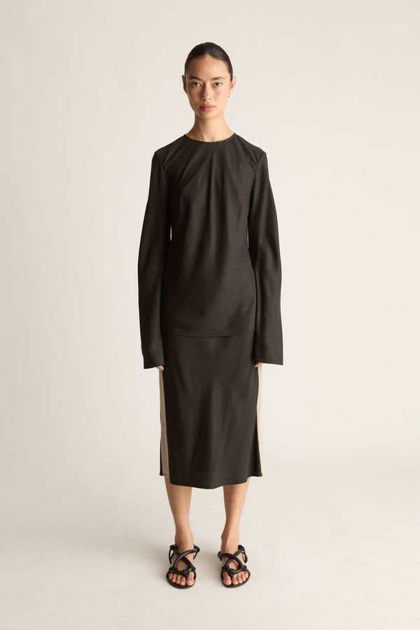 Front view of a woman wearing a black long sleeve shirt with a black skirt against a white studio background.