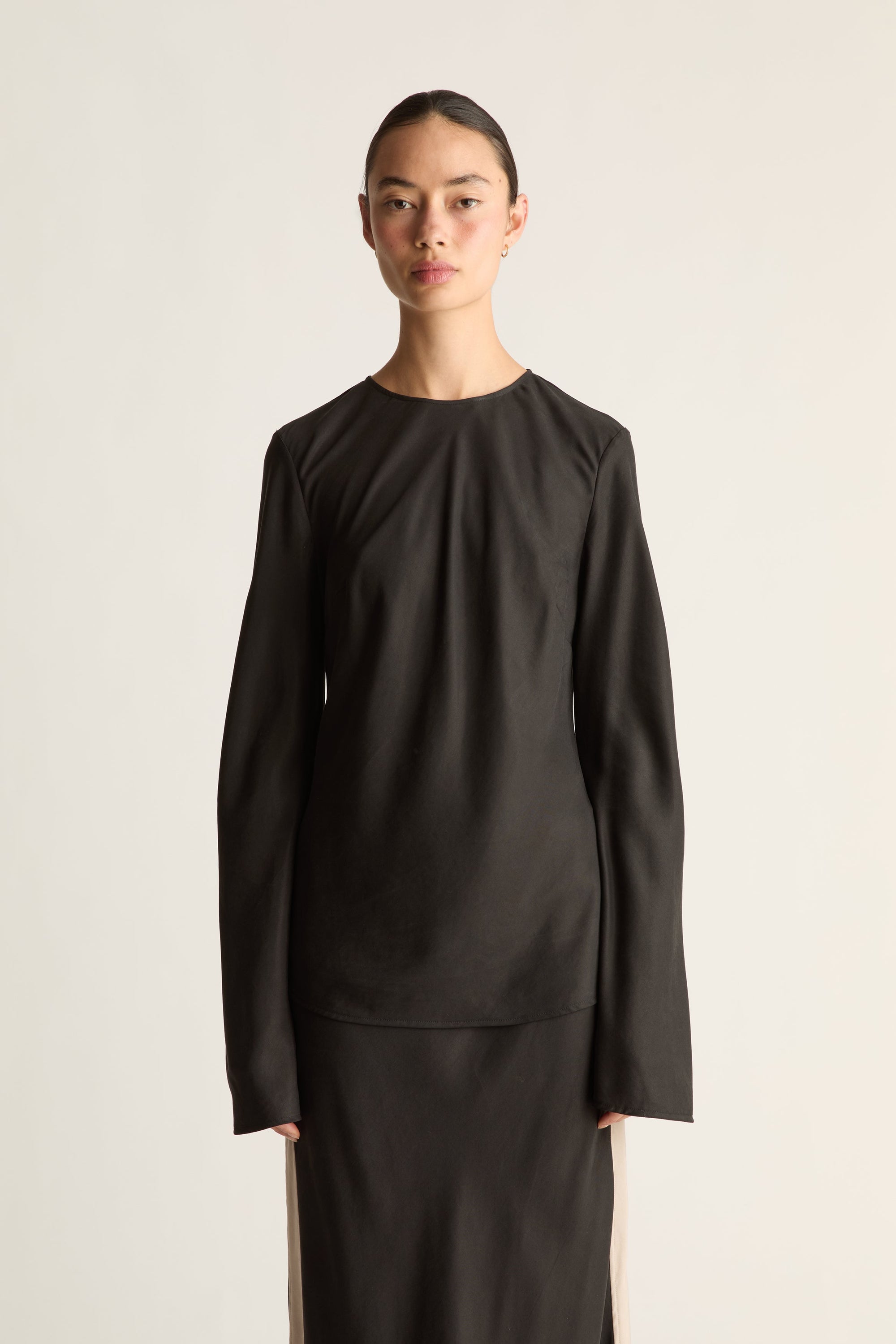 A woman wearing a black long sleeve shirt and skirt against a white studio background.