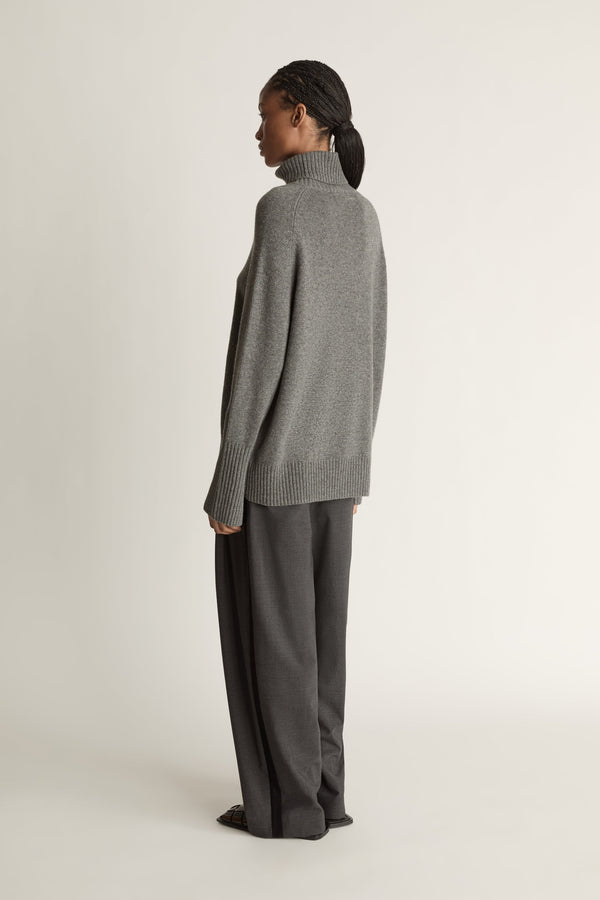 Woman wearing a gray turtleneck sweater and pants on a white background