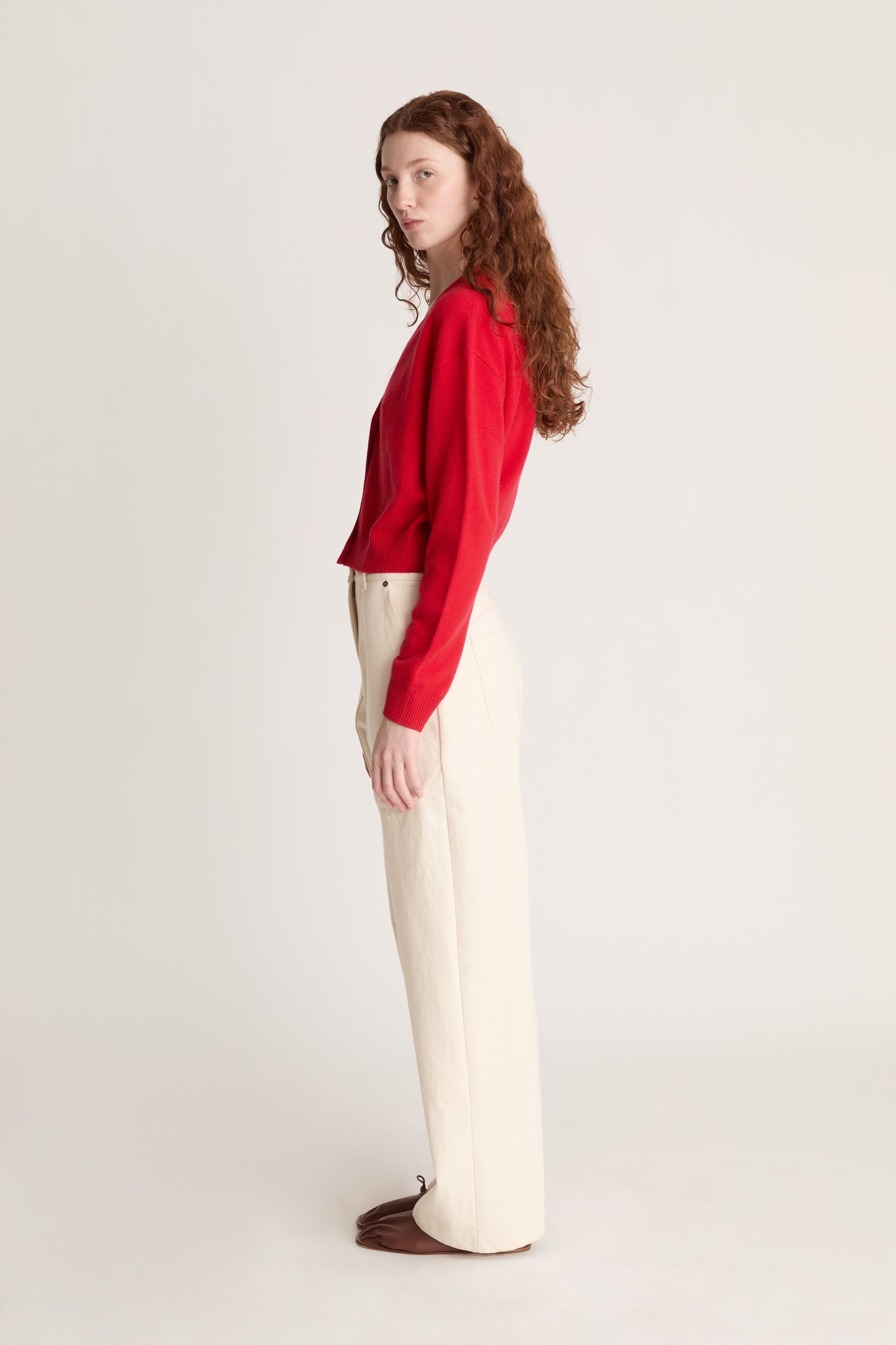 Woman wearing a red cardigan and white pants on a plain background