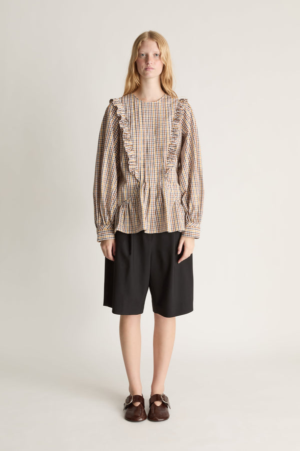 Front view of a person wearing a plaid shirt with ruffles and black shorts on a white background.
