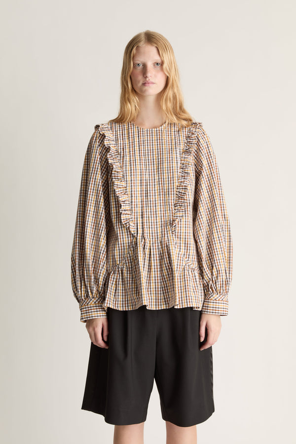 Close-up of a woman wearing a plaid blouse with ruffled details and black shorts on a plain background