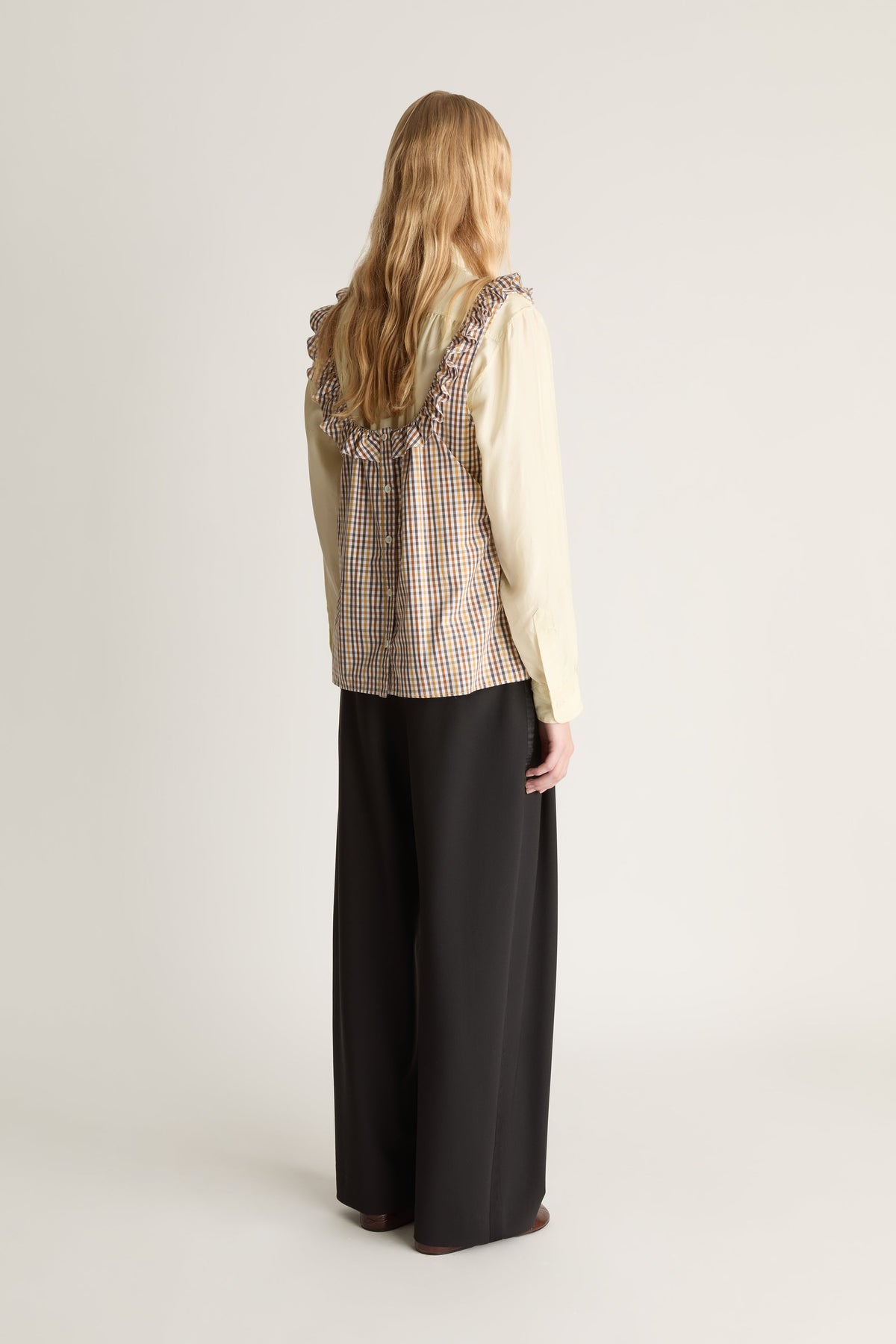 Back view of a person wearing a plaid shirt and black pants with a backpack on a white background