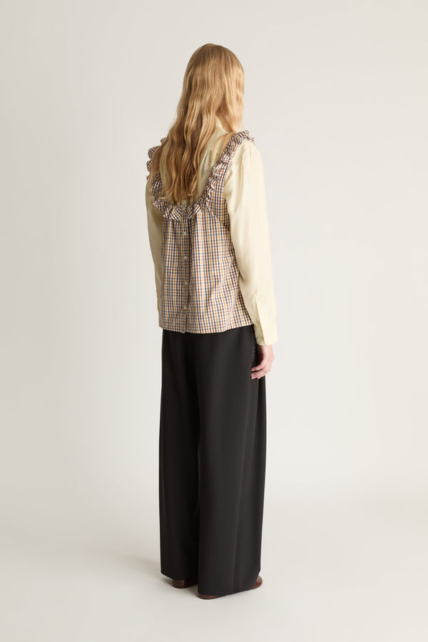 Back view of a person wearing a plaid shirt and black pants with a backpack on a white background