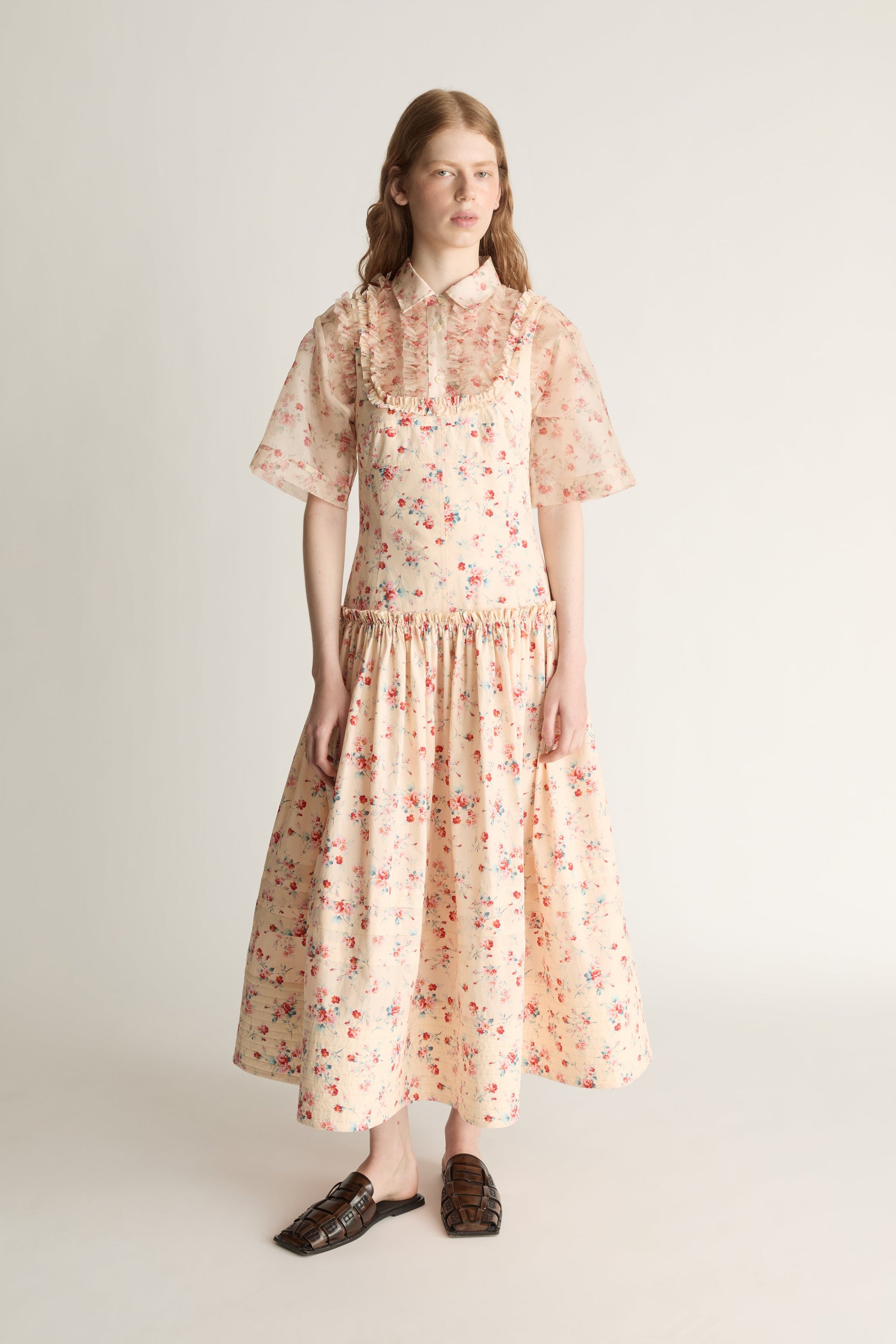 Woman wearing a floral dress over a shirt on a plain background