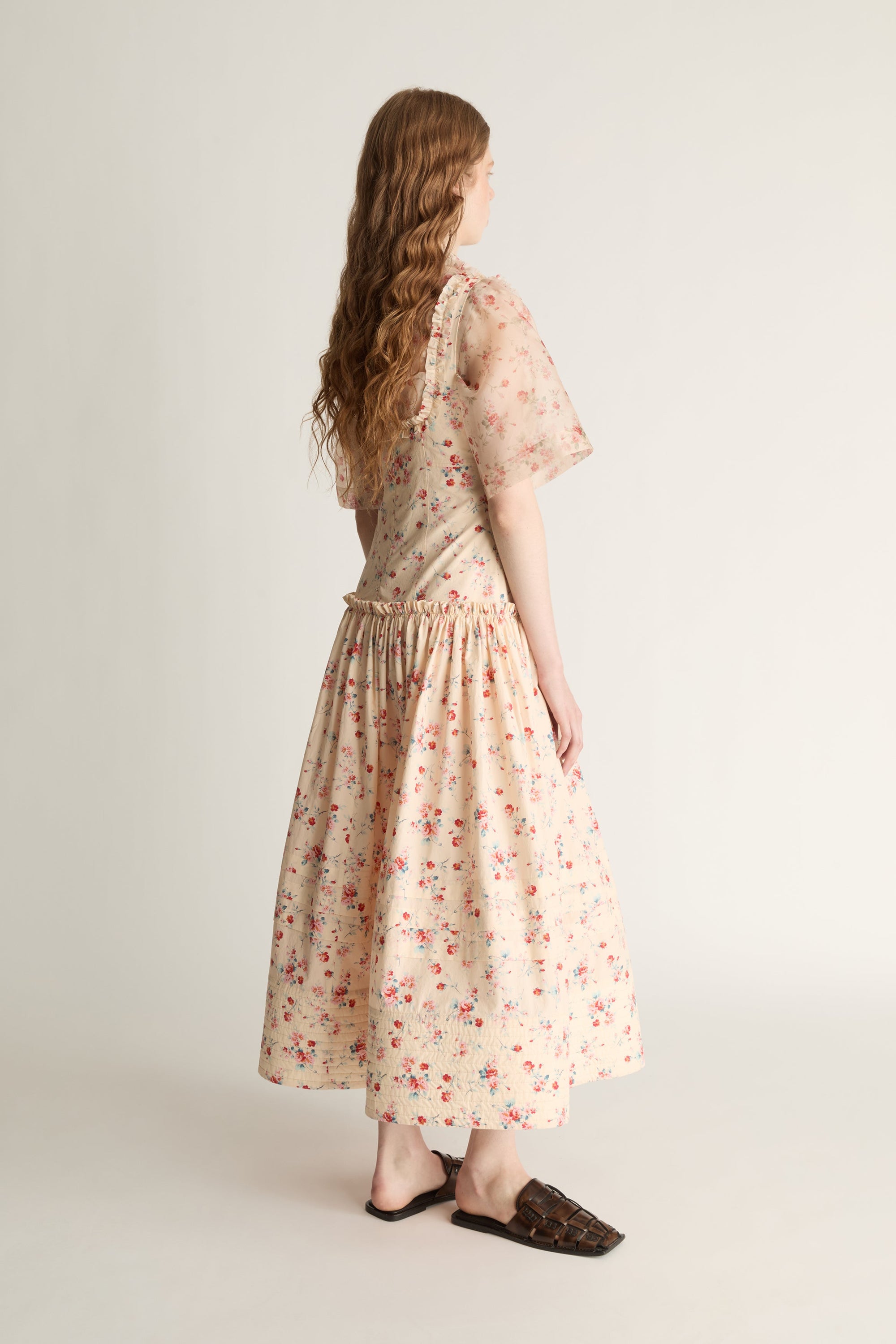 Woman wearing a floral dress over a shirt on a plain background