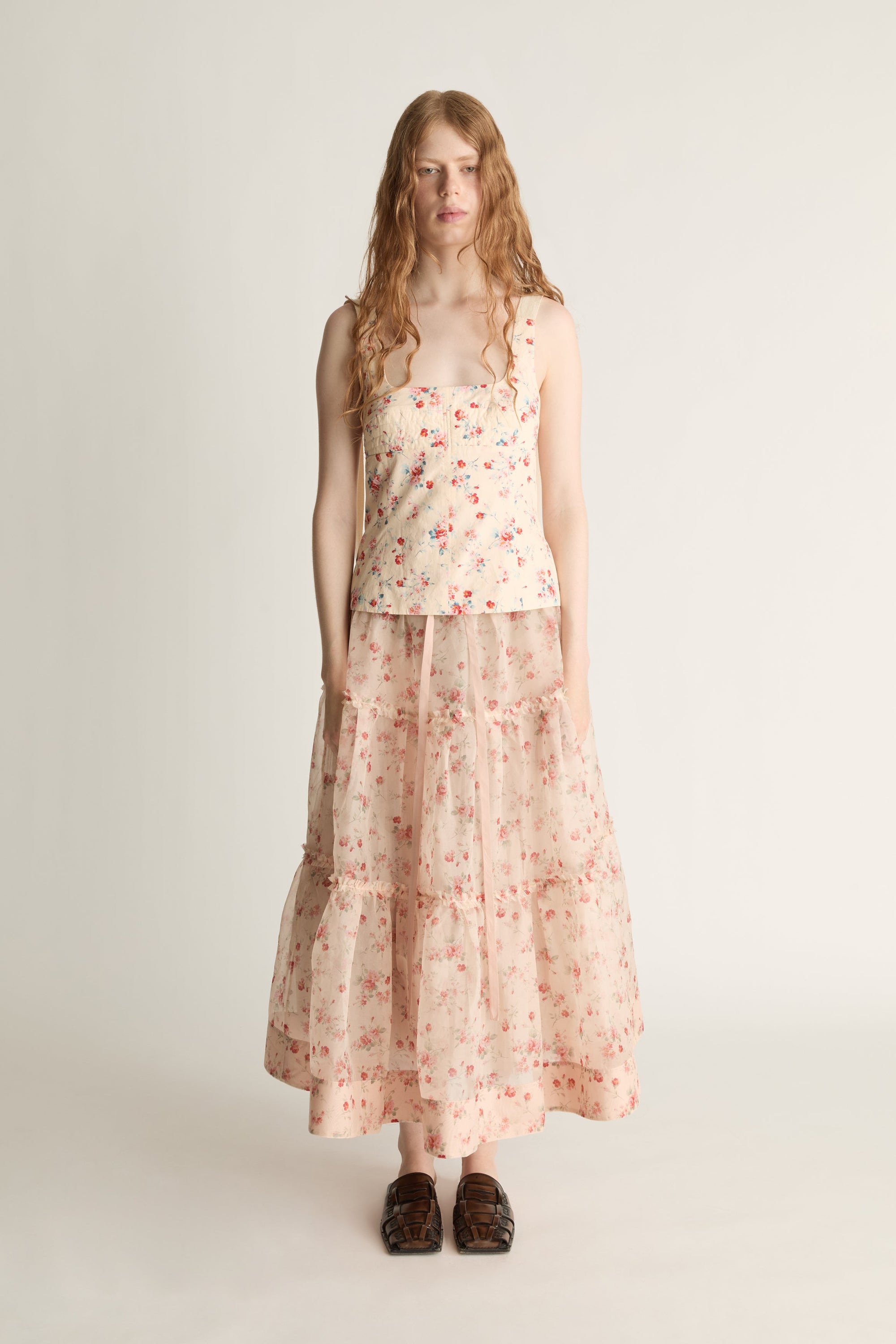 A woman wearing a floral top and skirt on a plain background