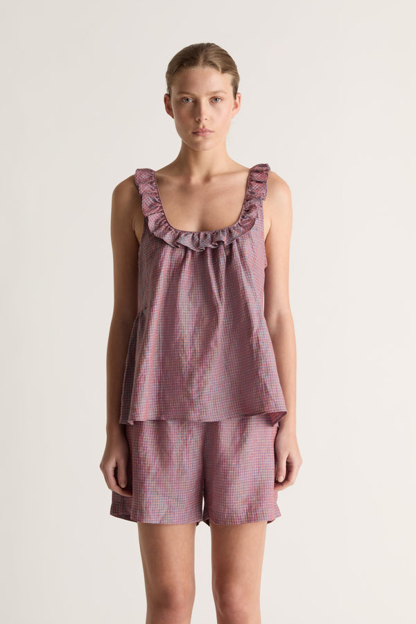 Close-up of a woman in plum check relaxed shorts and a matching sleeveless top with a ruffled scoop neckline