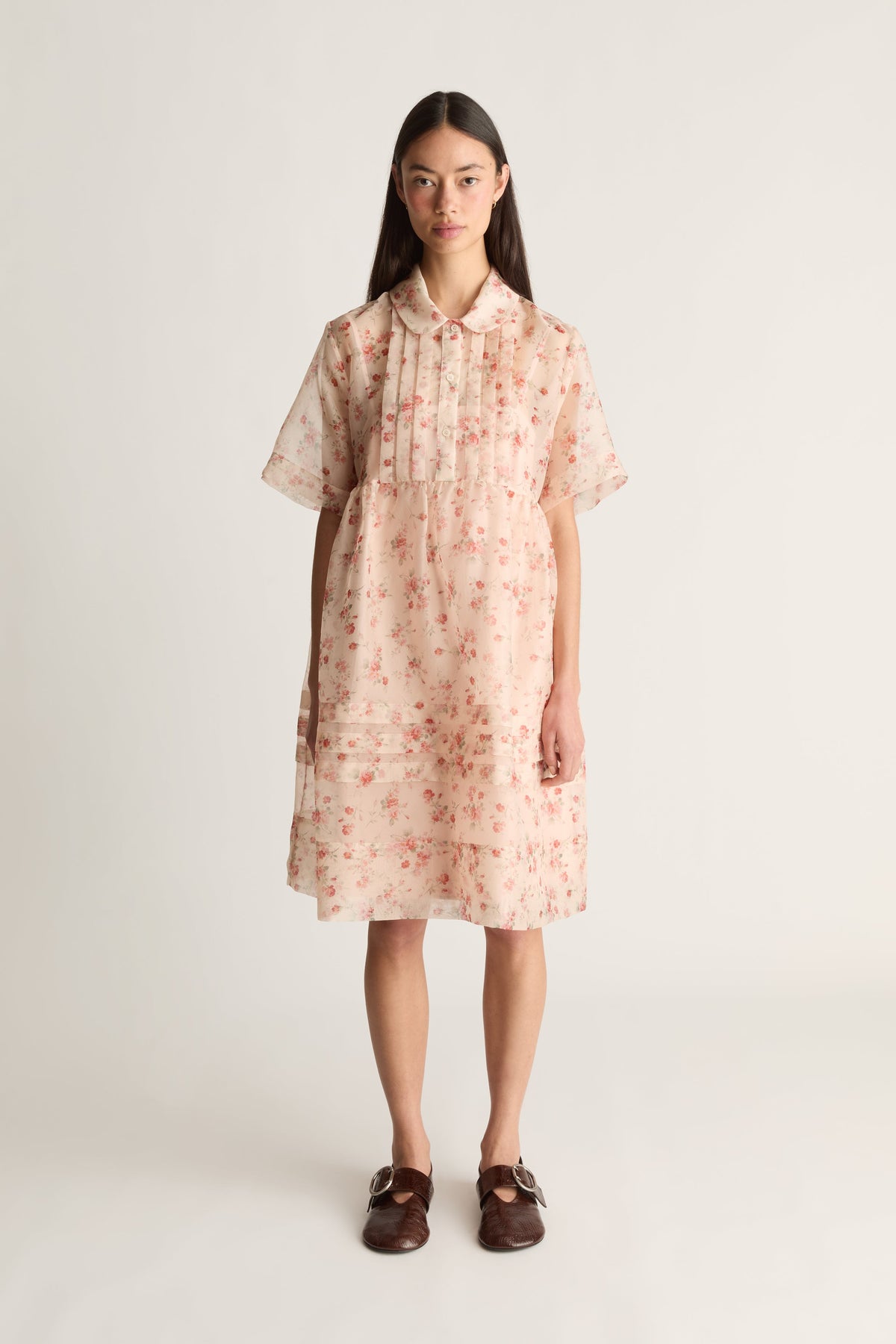 A front view image of a woman wearing a floral mini dress on a white background