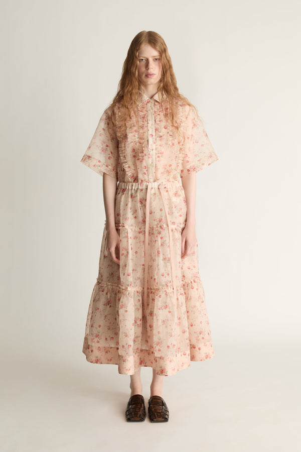 A woman wearing a floral shirt and skirt on a plain background