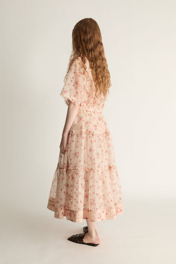 A woman wearing a floral shirt and skirt on a plain background