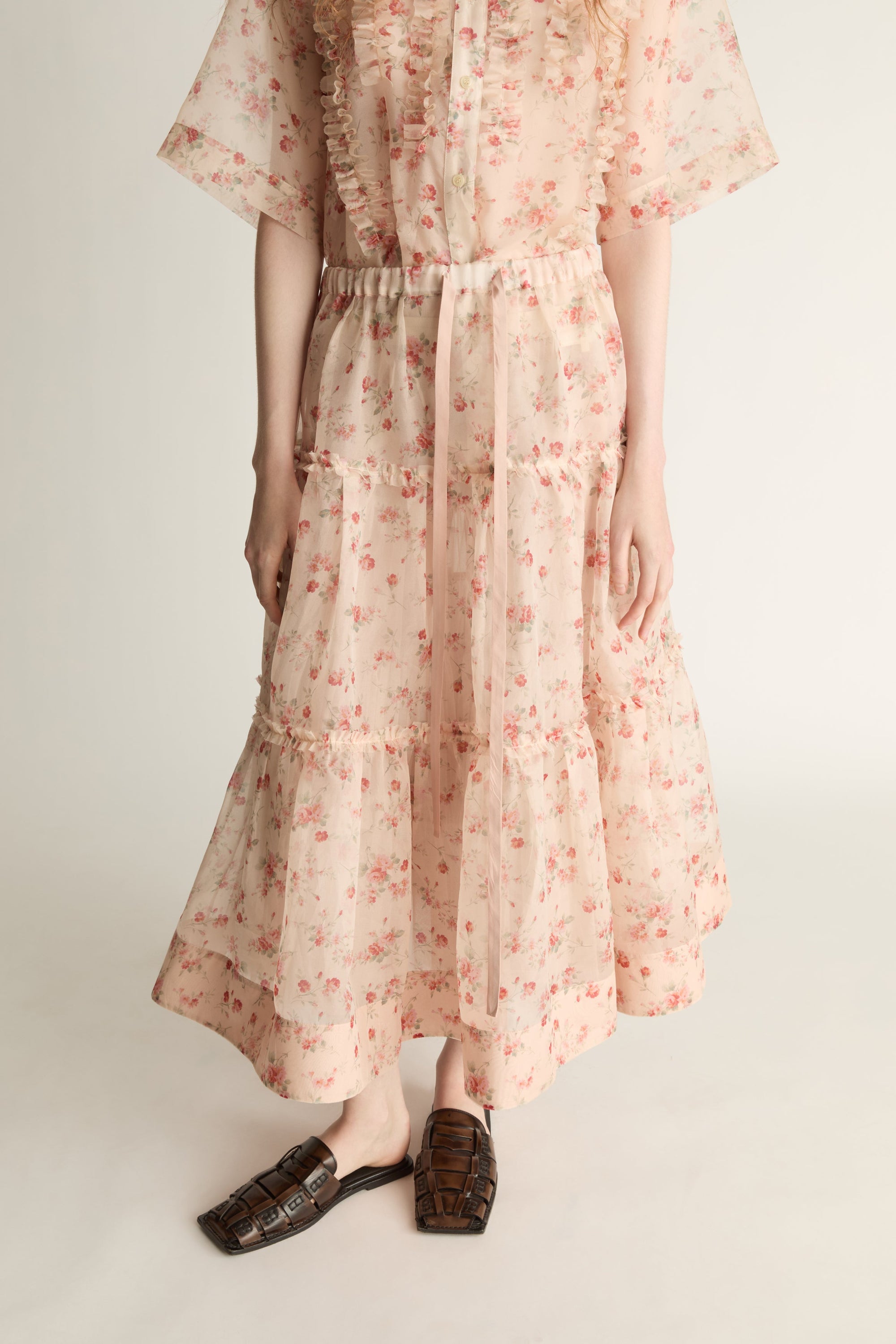 A woman wearing a floral shirt and skirt on a plain background