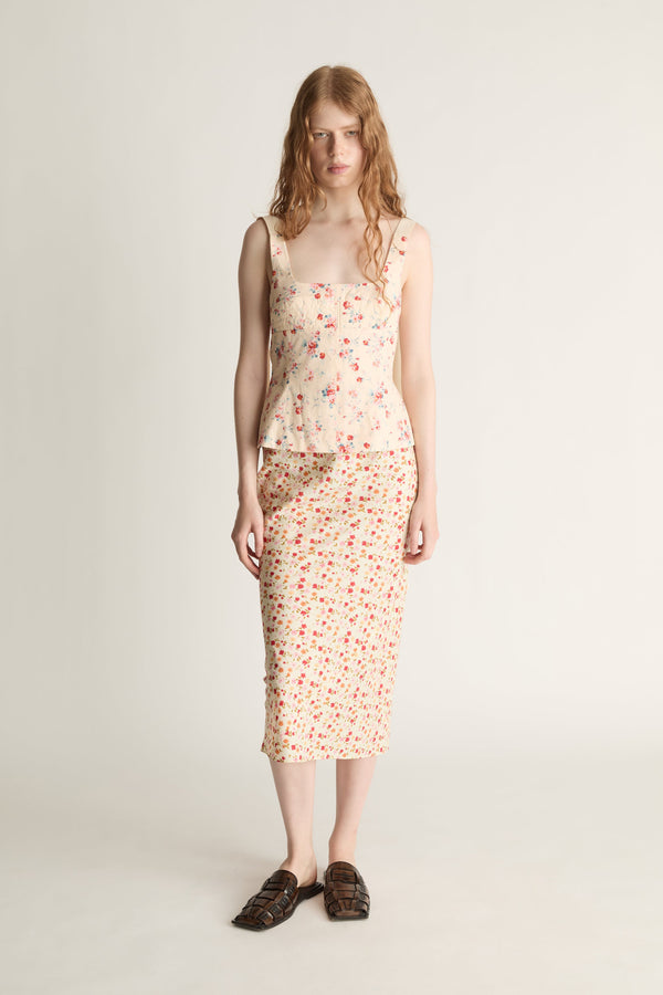 Woman wearing a floral blouse and slip skirt on a plain background
