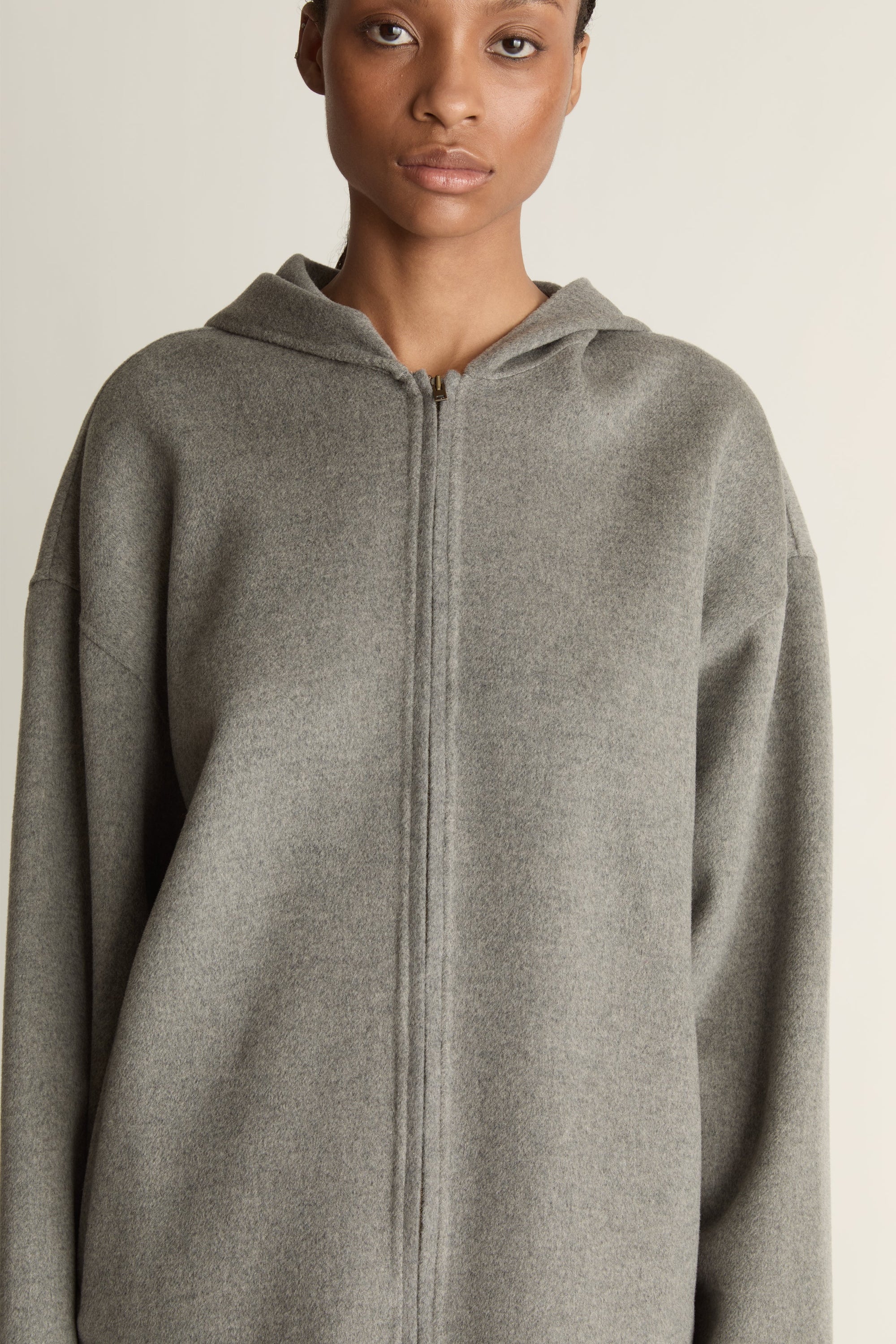 Person wearing a gray hoodie and plaid skirt on a plain background