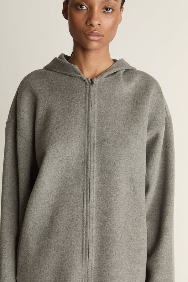Person wearing a gray hoodie and plaid skirt on a plain background