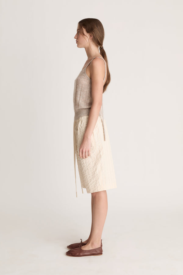 Woman wearing a beige knit cami top and cream coloured shorts on a white background