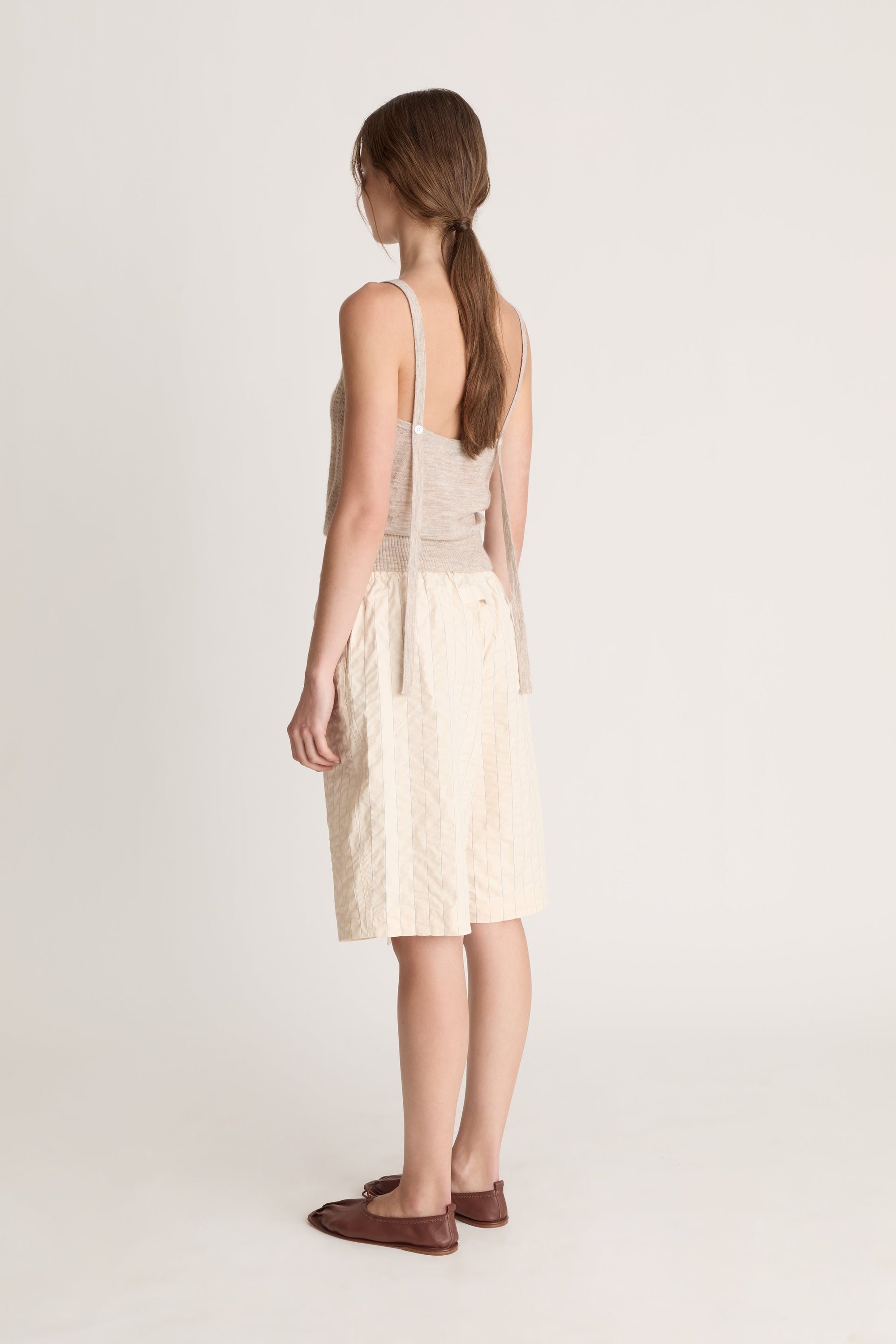 Woman wearing a beige knit cami top and cream coloured shorts on a white background