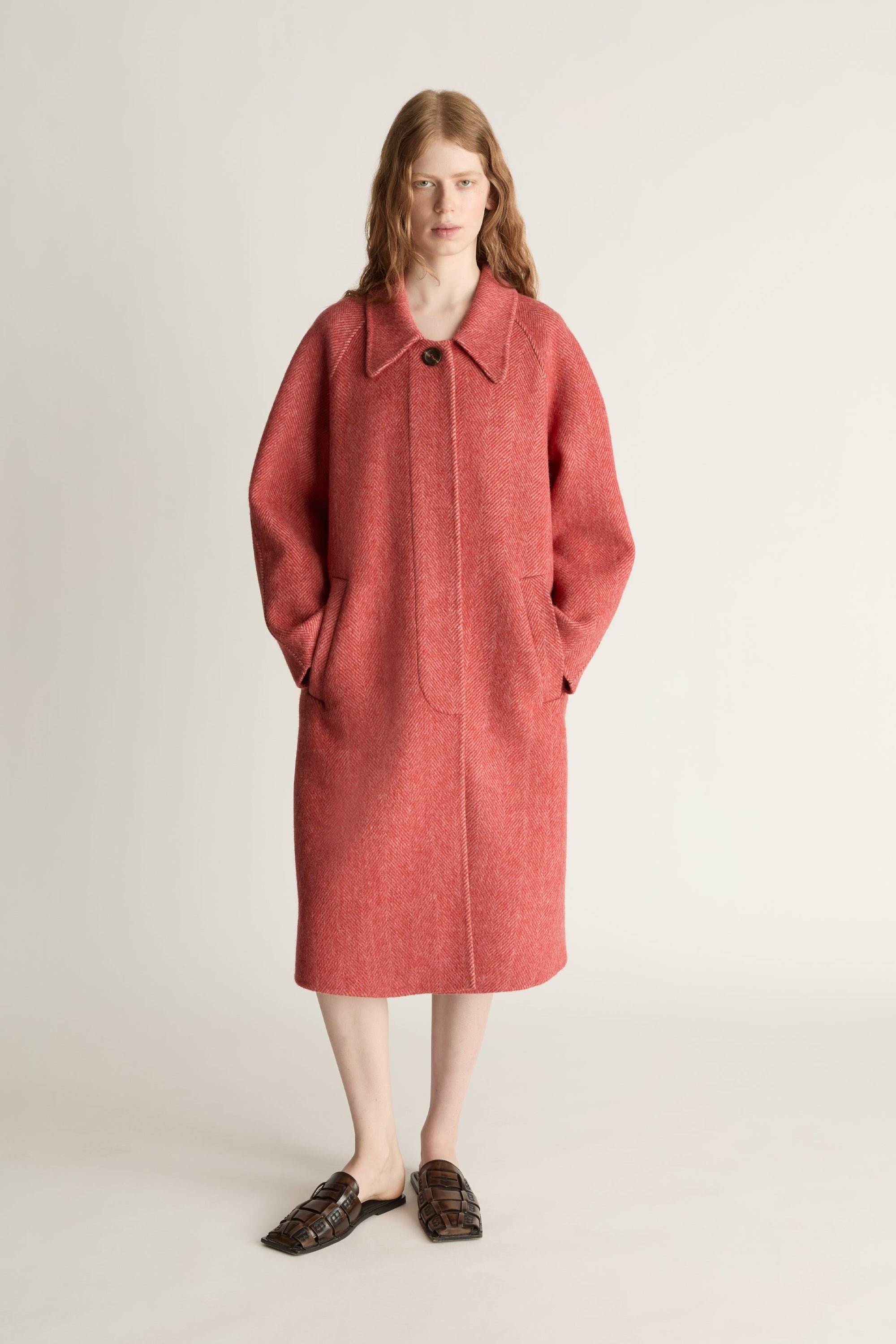 Woman wearing a long red coat on a plain background