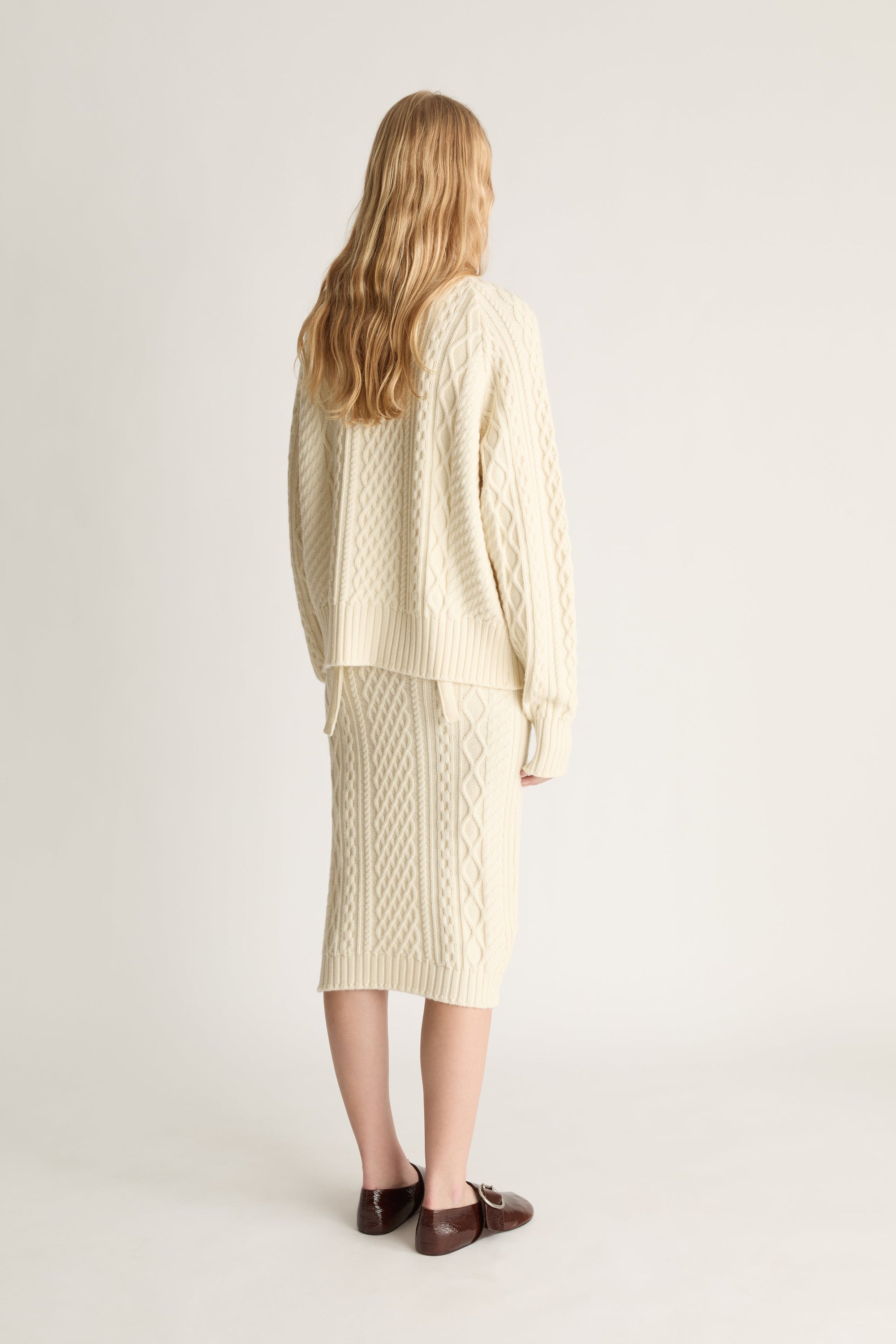 Person wearing a cream-colored cable knit sweater and skirt set on a white background