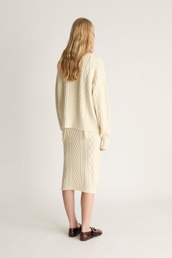 Person wearing a cream-colored cable knit sweater and skirt set on a white background