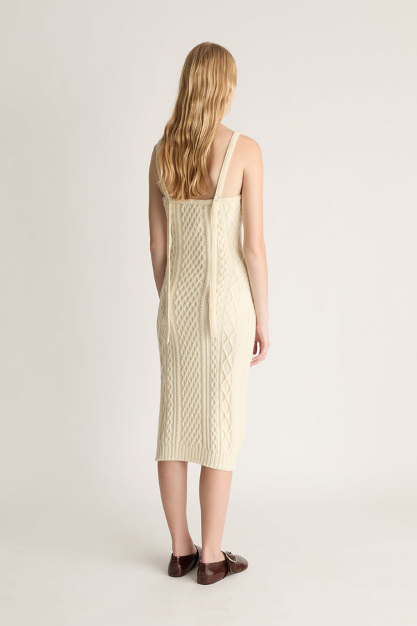 Back view of a woman wearing a cream-colored cable knit dress on on a white background
