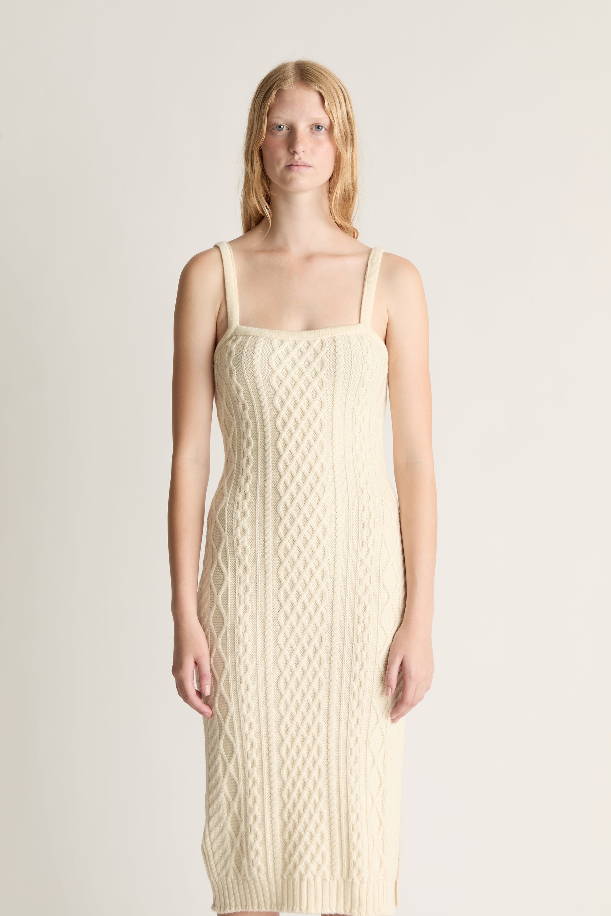Woman wearing a beige cable knit dress against a plain background