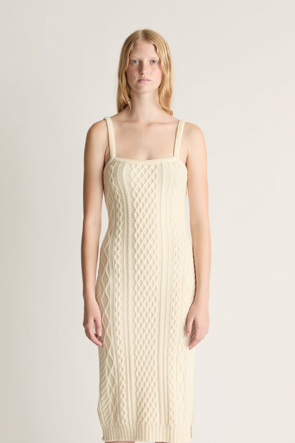 Woman wearing a beige cable knit dress against a plain background