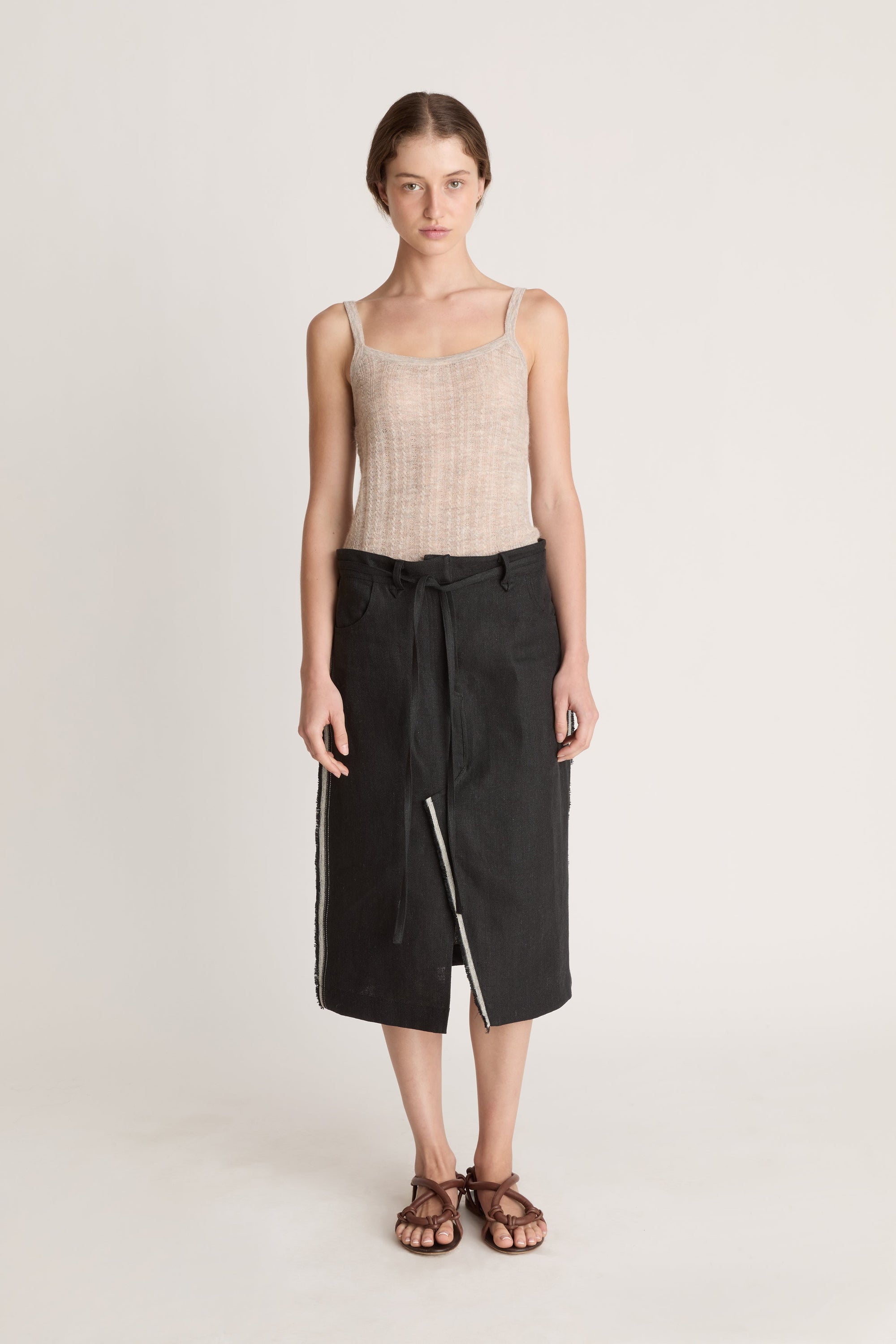 Woman wearing a beige tank top and black wrap skirt on a white background