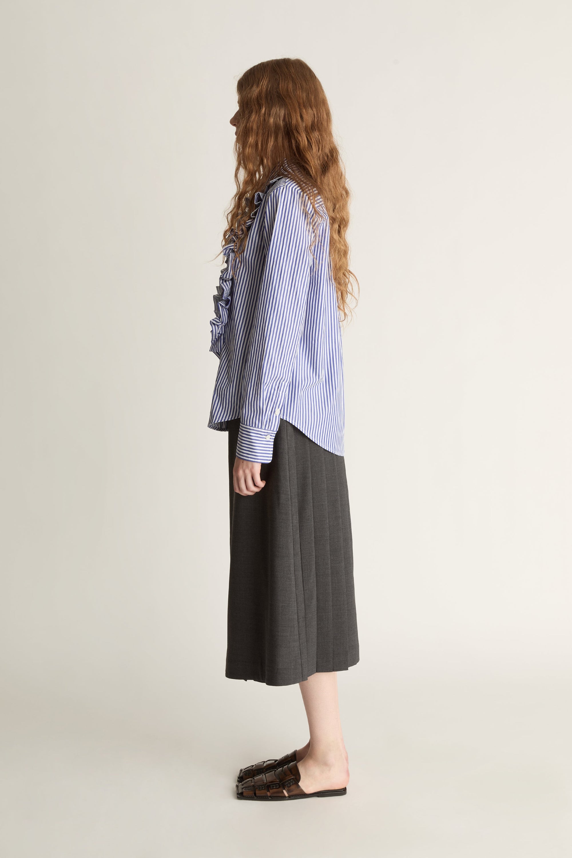 Woman wearing a blue striped shirt with ruffles and a gray skirt on a white background