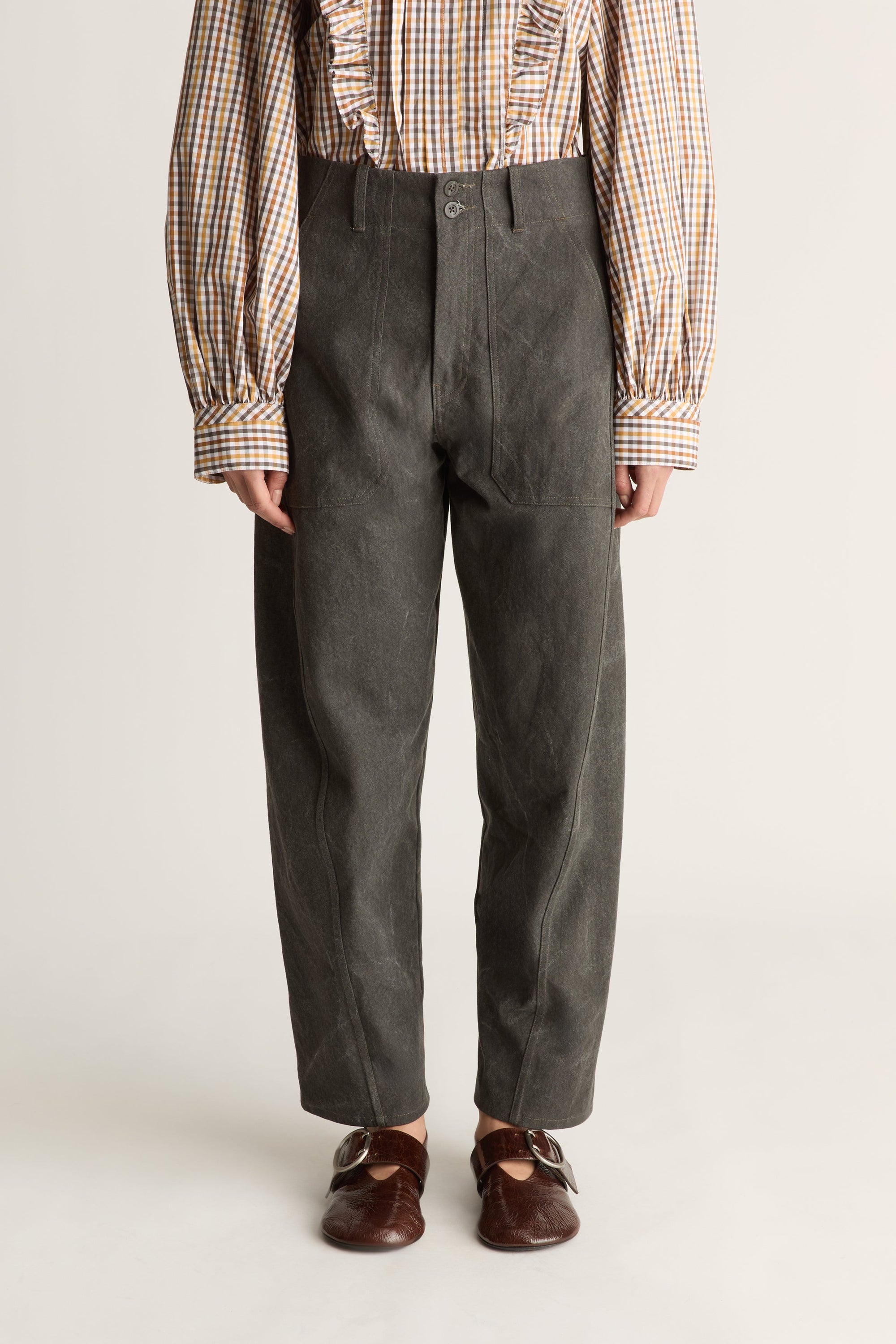 Close up of a woman wearing a checkered blouse and charcoal pants against a white studio background.